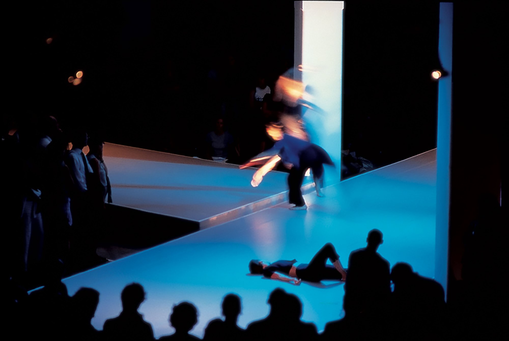Image: The audience surroud two dancers as they perform in a blur of motion under the blue lights of the Atlantis Building during 13 Different Keys, 1999. Photograph: Sarah Ainslie