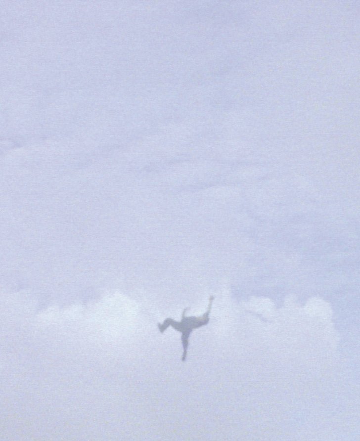 Still from Steve McQueen's Caribs' Leap, 2002 depicting a figure mid-flight against a cloudy sky.