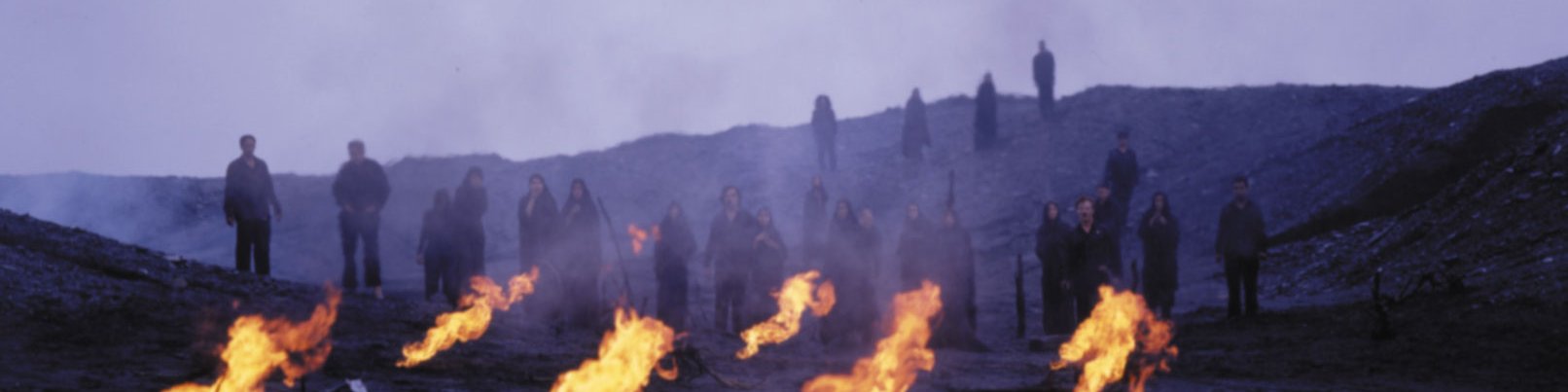 Image: Still from the film that formed part of the performance at The Union Chapel, featuring Sussan Deyhim and a choir, emerge from the charred horizon, obscured by smoke and flames in the foreground. Still: Shoja Azari, Sussan Deyhim, Ghasem Ebrahimian and Shirin Neshat