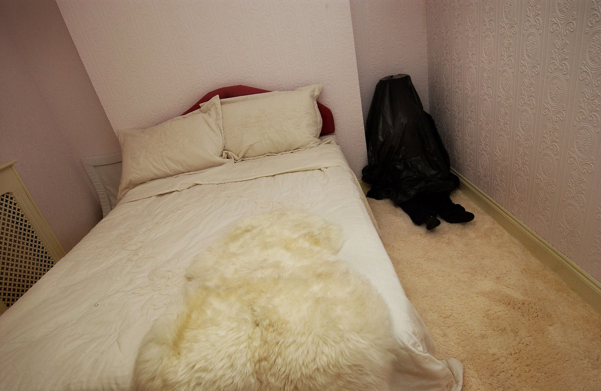 A child like figure  concealed by a bin bag sits in the corner of a bedroom in Walden Street during Die Familie Schneider, 2004.