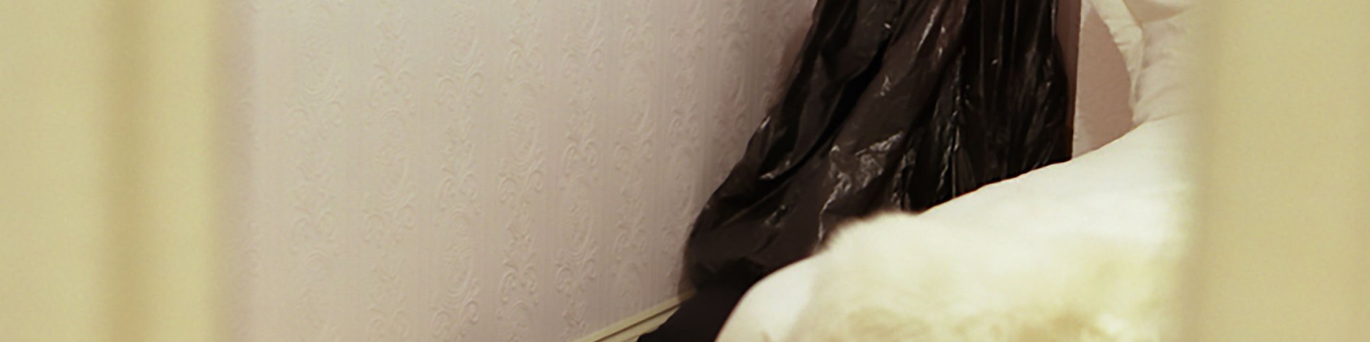 A child like figure  concealed by a bin bag sits in the corner of a bedroom in Walden Street during Die Familie Schneider, 2004.