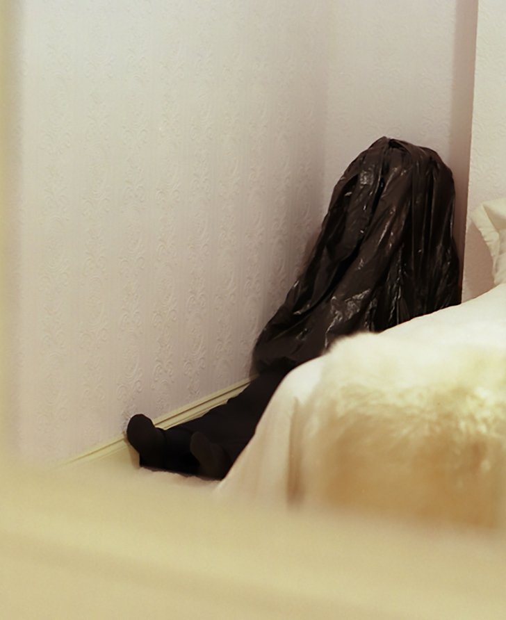 A child like figure  concealed by a bin bag sits in the corner of a bedroom in Walden Street during Die Familie Schneider, 2004.