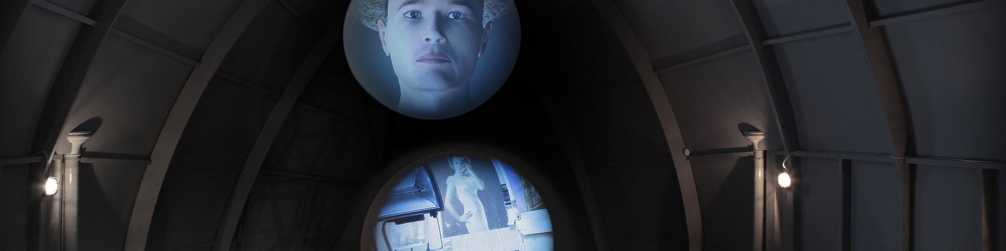 Image: Computer generated animations of a man and a room are projected onto two screens, concave and convex, as installed in The Tin Tabernacle, Kilburn, during Nowhere Less Now, 2012. Photograph: Lindsay Seers