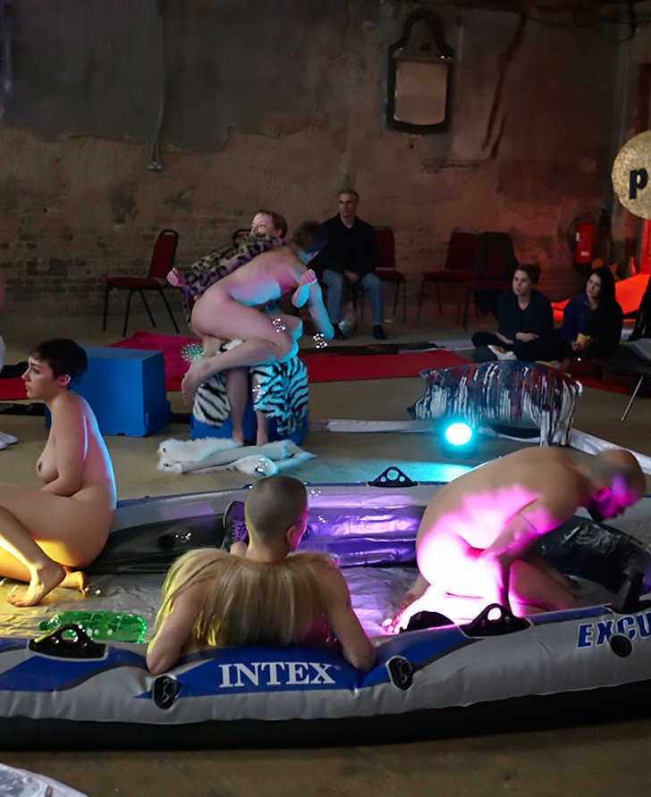 Image: Three naked performers lie in a dinghy while two pairings of performers in various states of undress sit on upturned blue boxes closer to the audience at the ASYLUM Peckam party, 4 May 2013.