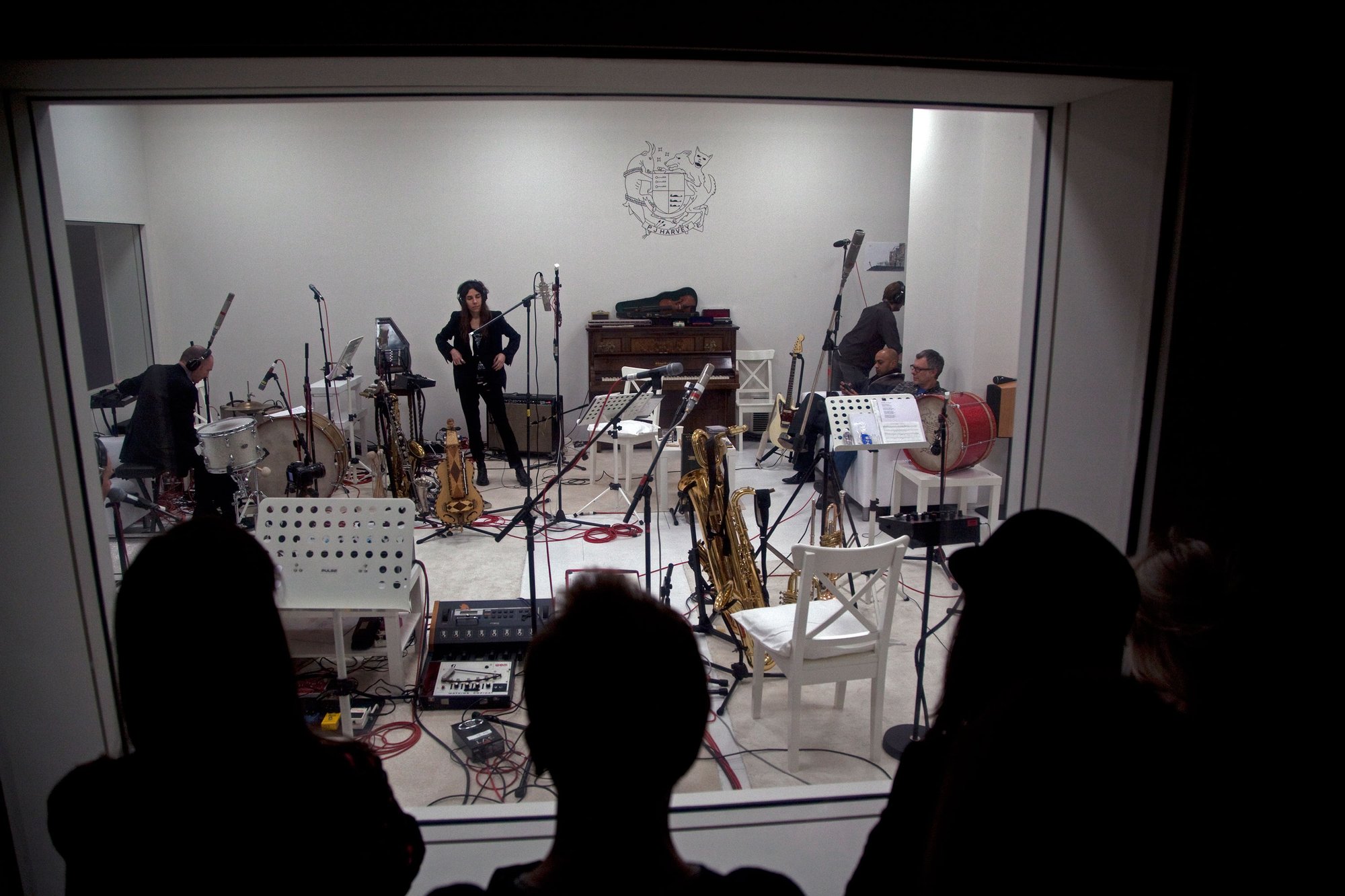 Image: PJ Harvey and musicians rehearse amongst cables, pedals and instruments including drum kit, saxophone, autoharp and ornate hurdy gurdy in the pristine white recording studio as audience members watch through one-way glass at Somerset House, January, 2015. Photograph: Stephen White