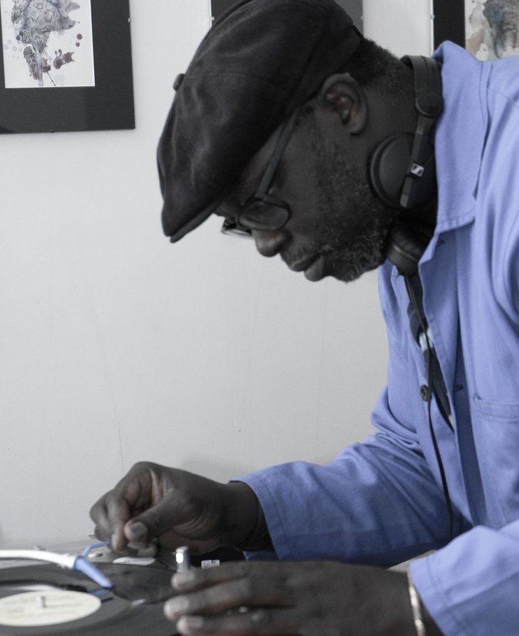 A desaturated image of Peter Adjaye concentrating on a turntable. 